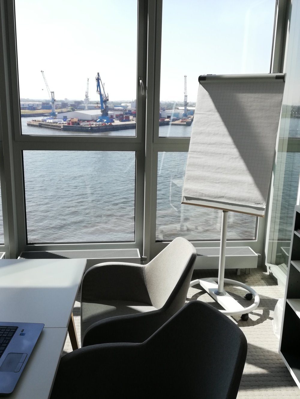 Besprechungsraum von STEINBACH STRATEGIEN mit Flipchart und Sesseln, Blick durch große Fenster auf Hafenkräne und Wasser